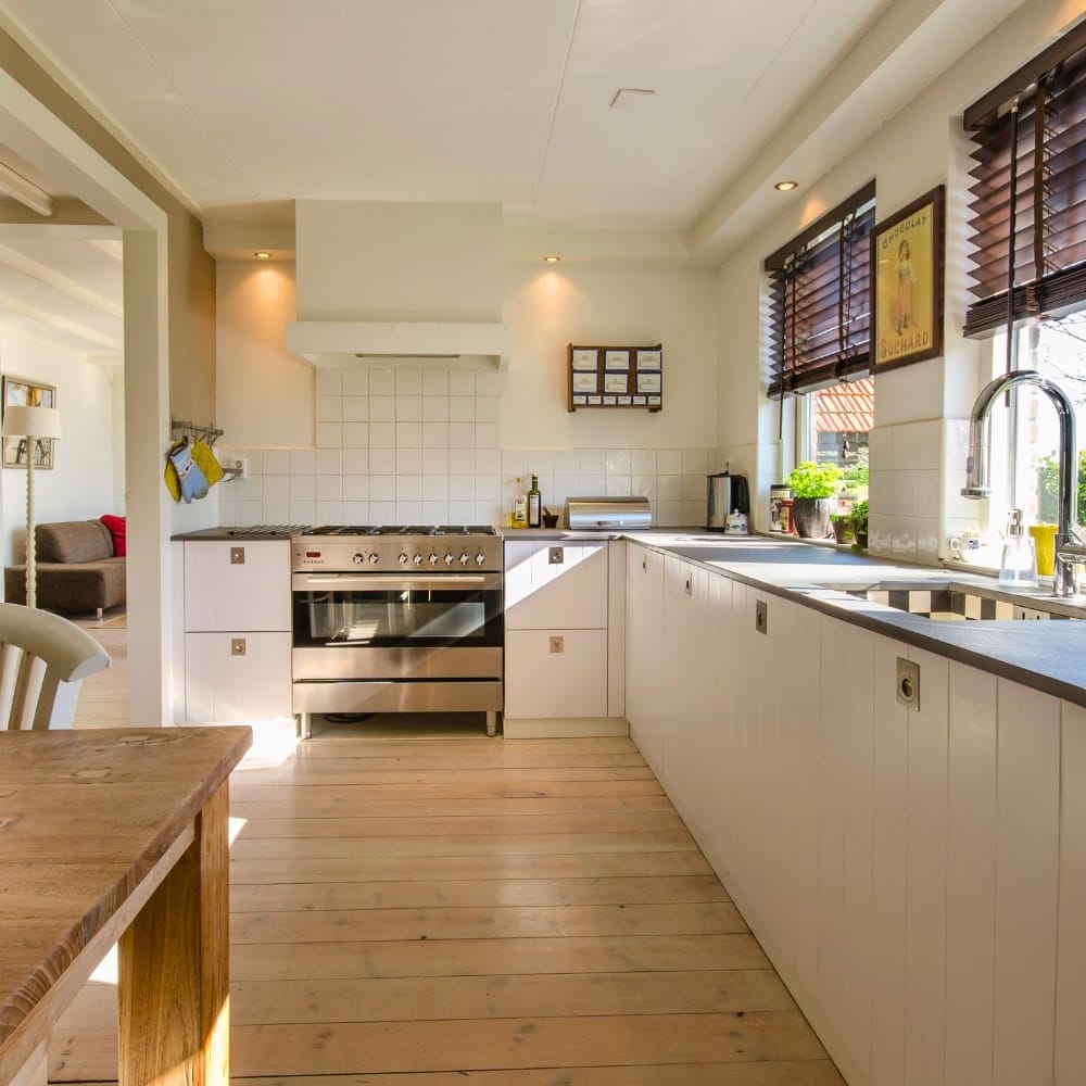 Sunny white kitchen with pine plank floor, stainless gas range, and wooden blinds