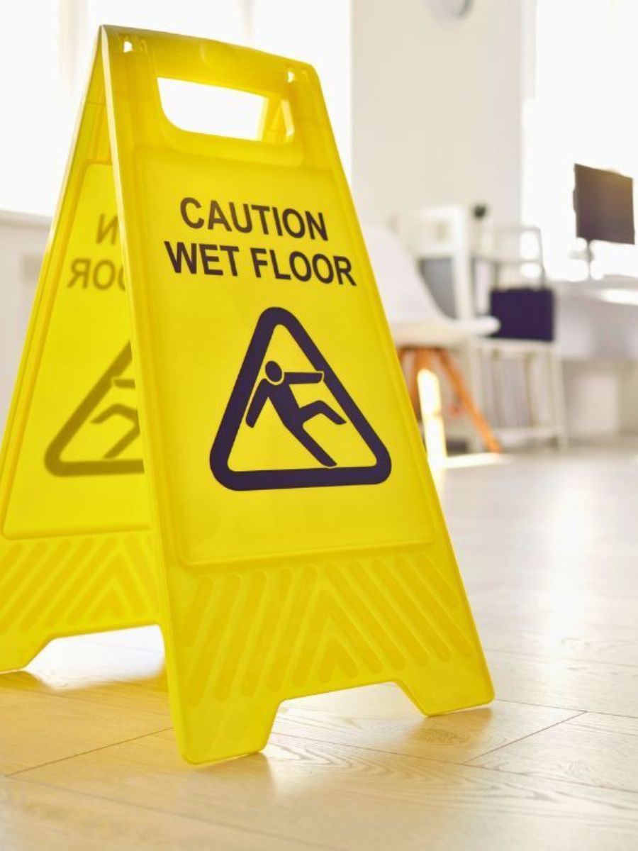 Yellow caution wet floor A-frame safety sign on a wood floor in a bright office