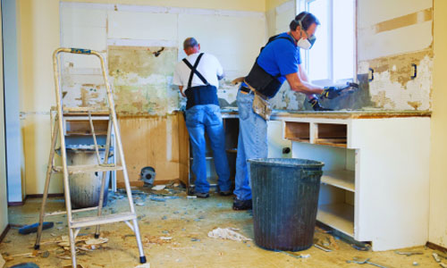Two workers in respirator masks and safety gear stripping a kitchen during lead abatement