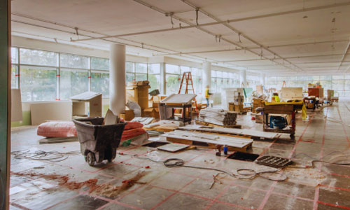 Empty commercial floor with construction debris, ladders, and paint splatter
