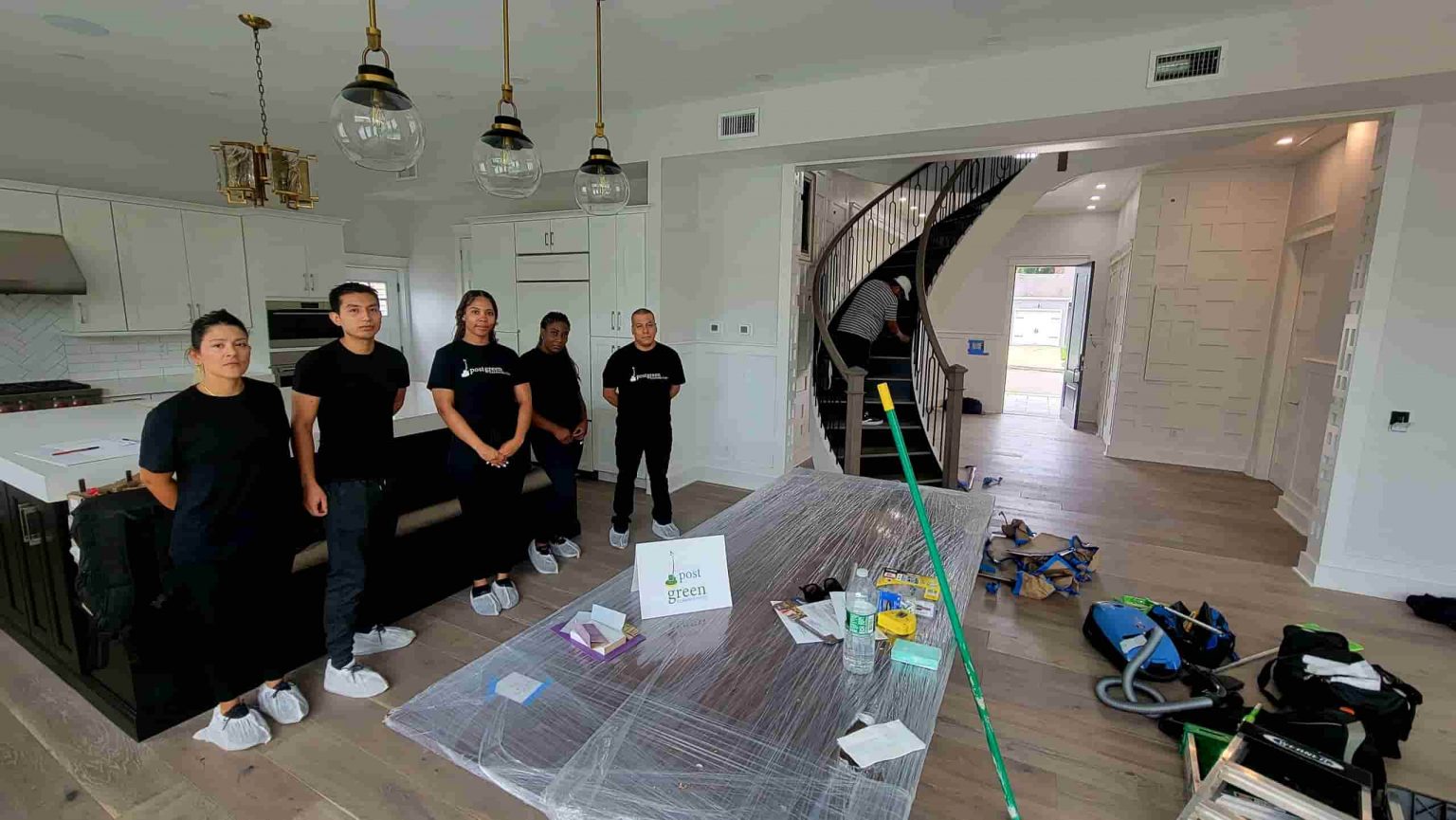 Five Post Green Cleaning technicians in black uniforms standing in a new-construction home with cleaning equipment