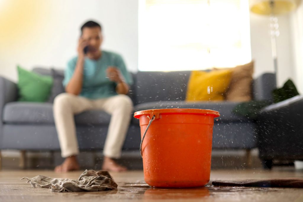Homeowner dealing with indoor water damage and flooding while calling for emergency basement flood cleanup and water damage restoration services